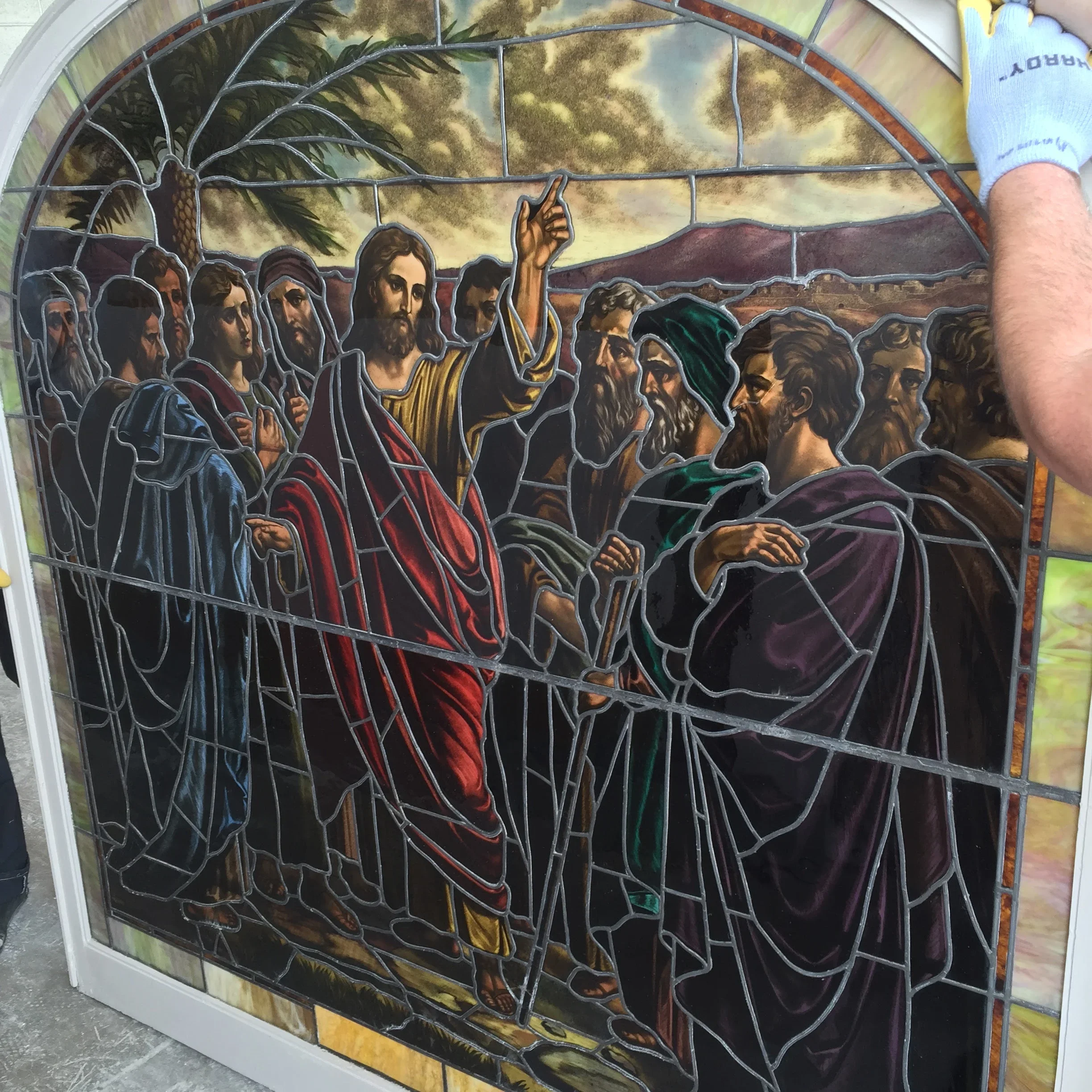 Arched stained glass window with religious figures in colorful robes and lead framing