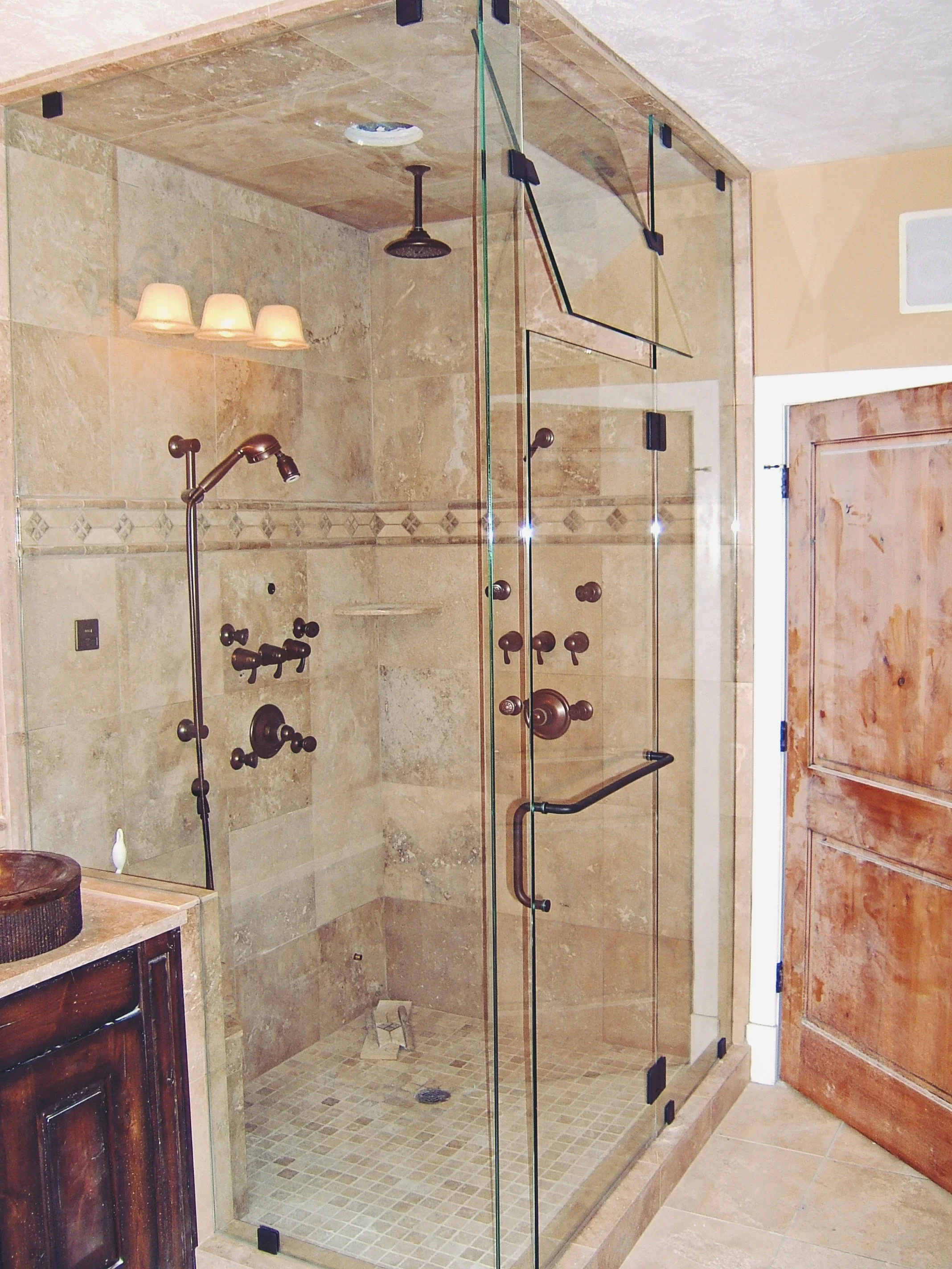 Frameless glass shower with travertine tile walls and bronze hardware in master bathroom