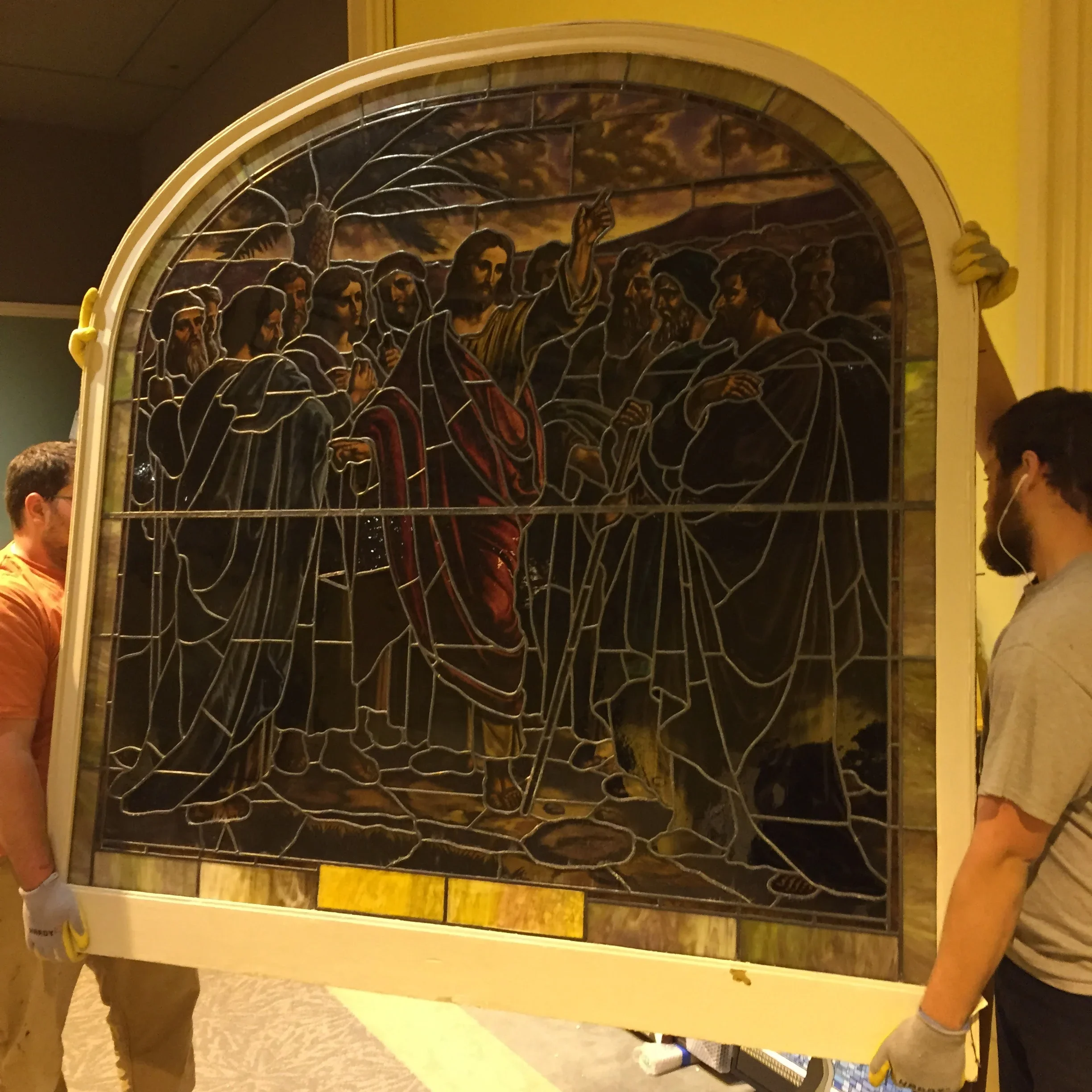 Large arched stained glass window with religious figures and lead detailing being installed