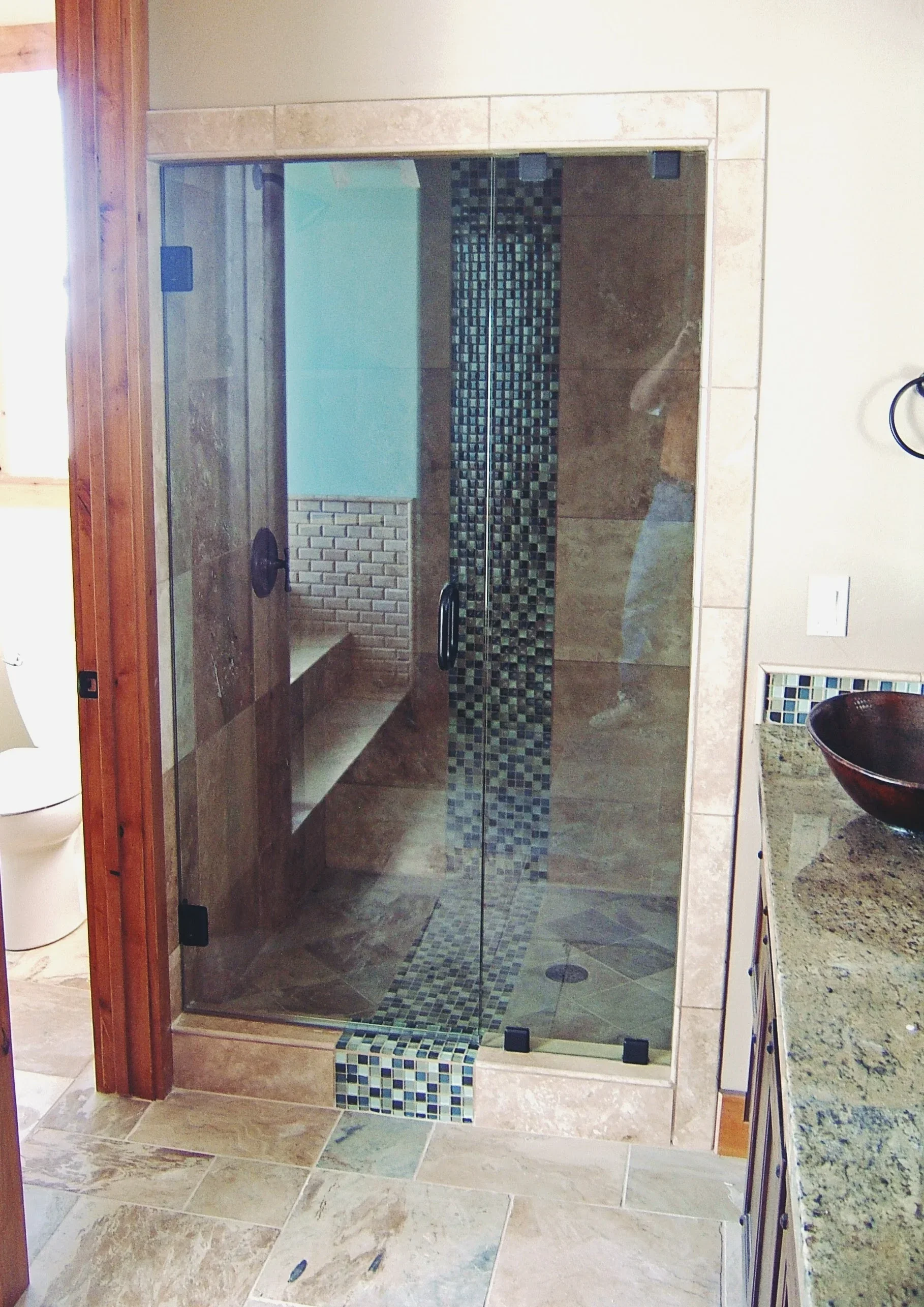 Frameless glass shower enclosure with mosaic tile accent and stone finishes