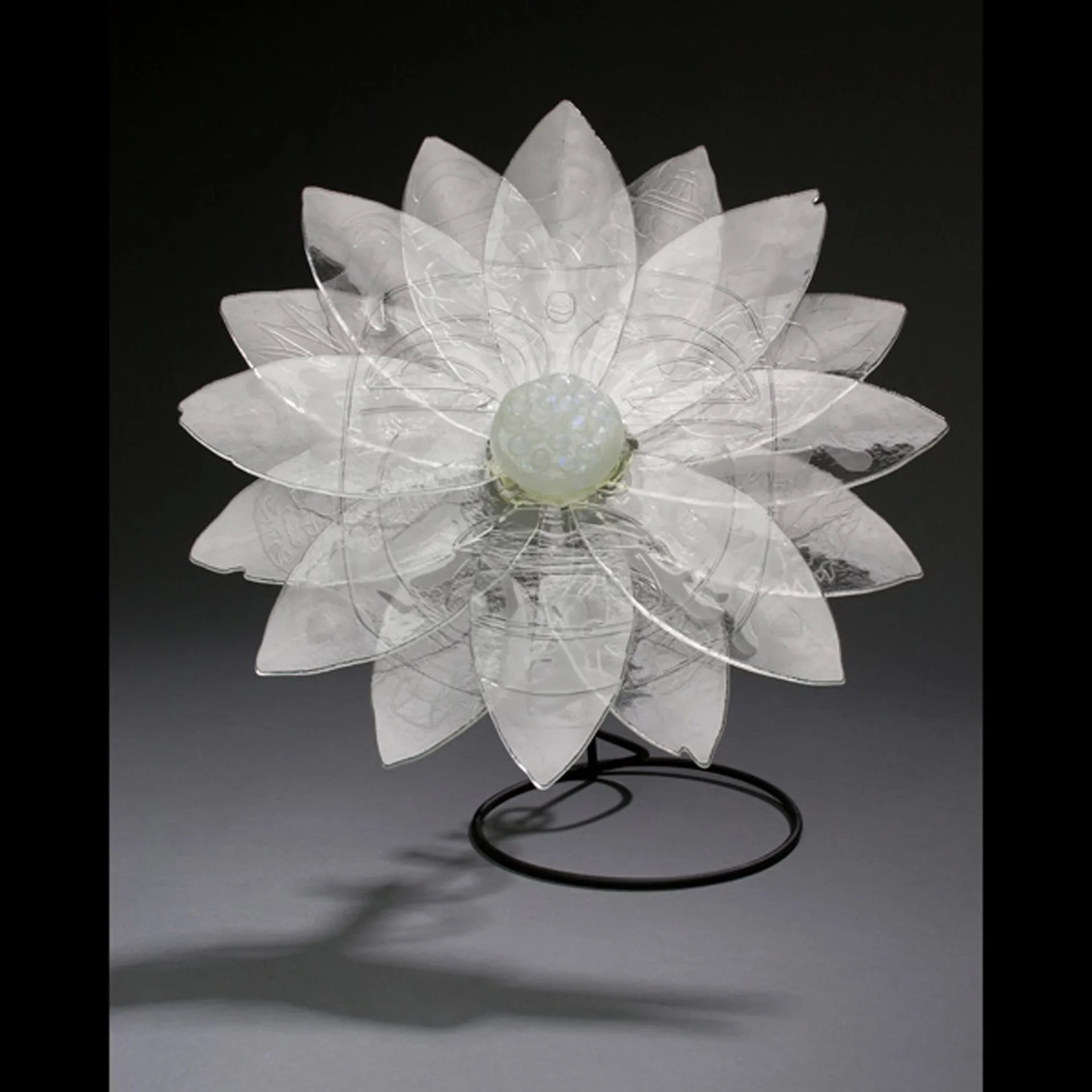 Etched glass lotus flower with translucent petals and jade center on black metal stand