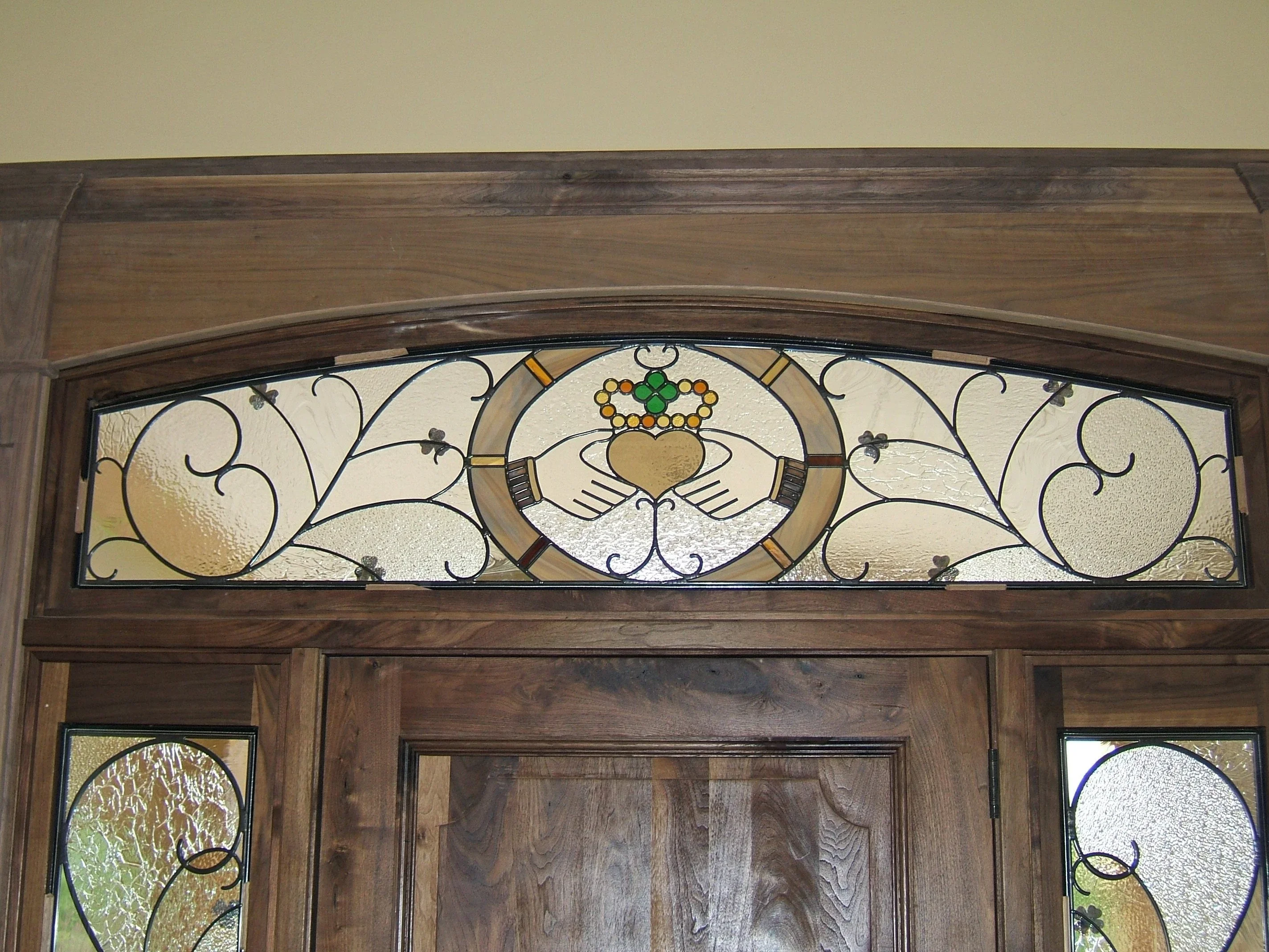Stained glass transom with Claddagh heart crown design in amber and clear glass above wooden door