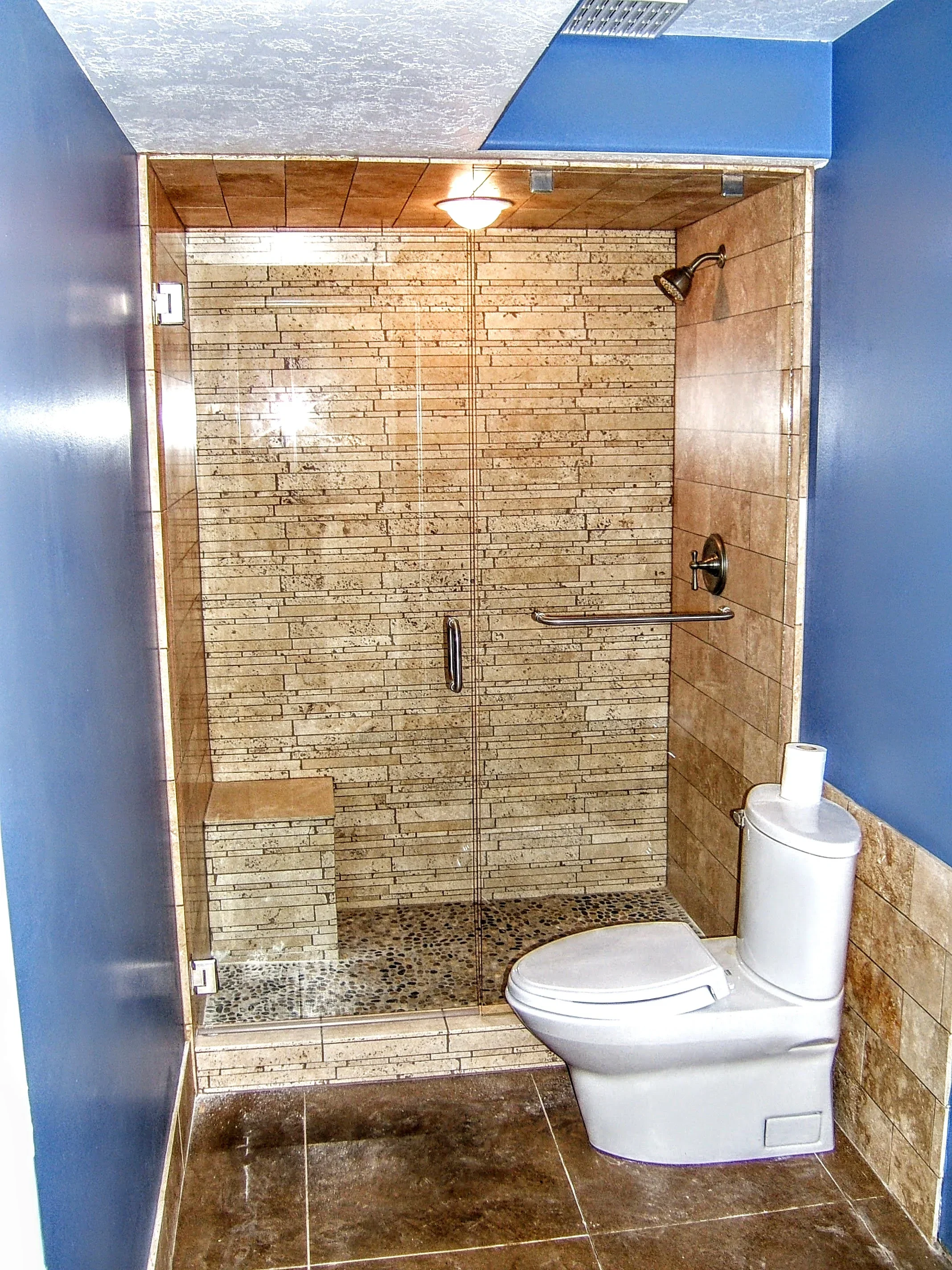 Frameless glass shower enclosure with stone tile walls and pebble floor in modern bathroom