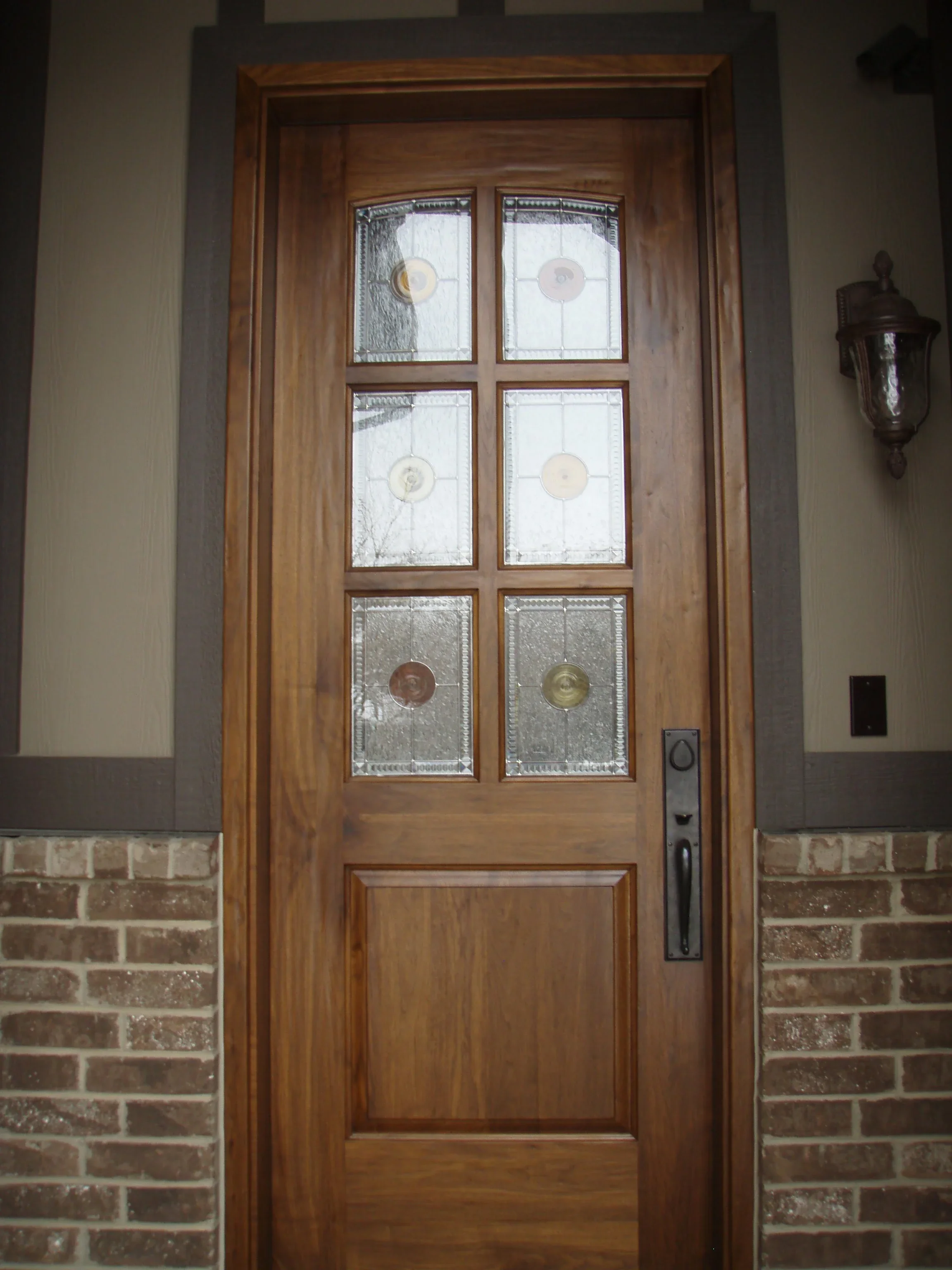 Wooden entry door with six beveled glass panels and brass hardware on brick exterior