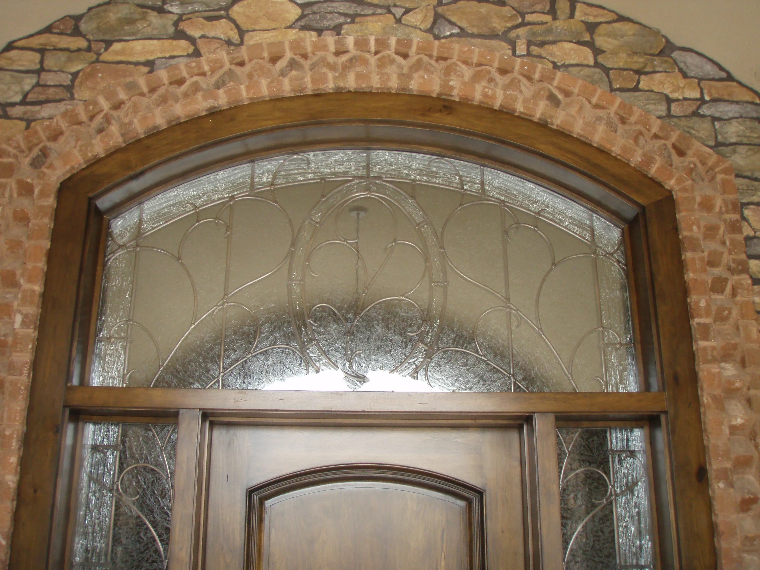 Arched decorative glass transom window with beveled pattern above wooden entry door in brick archway