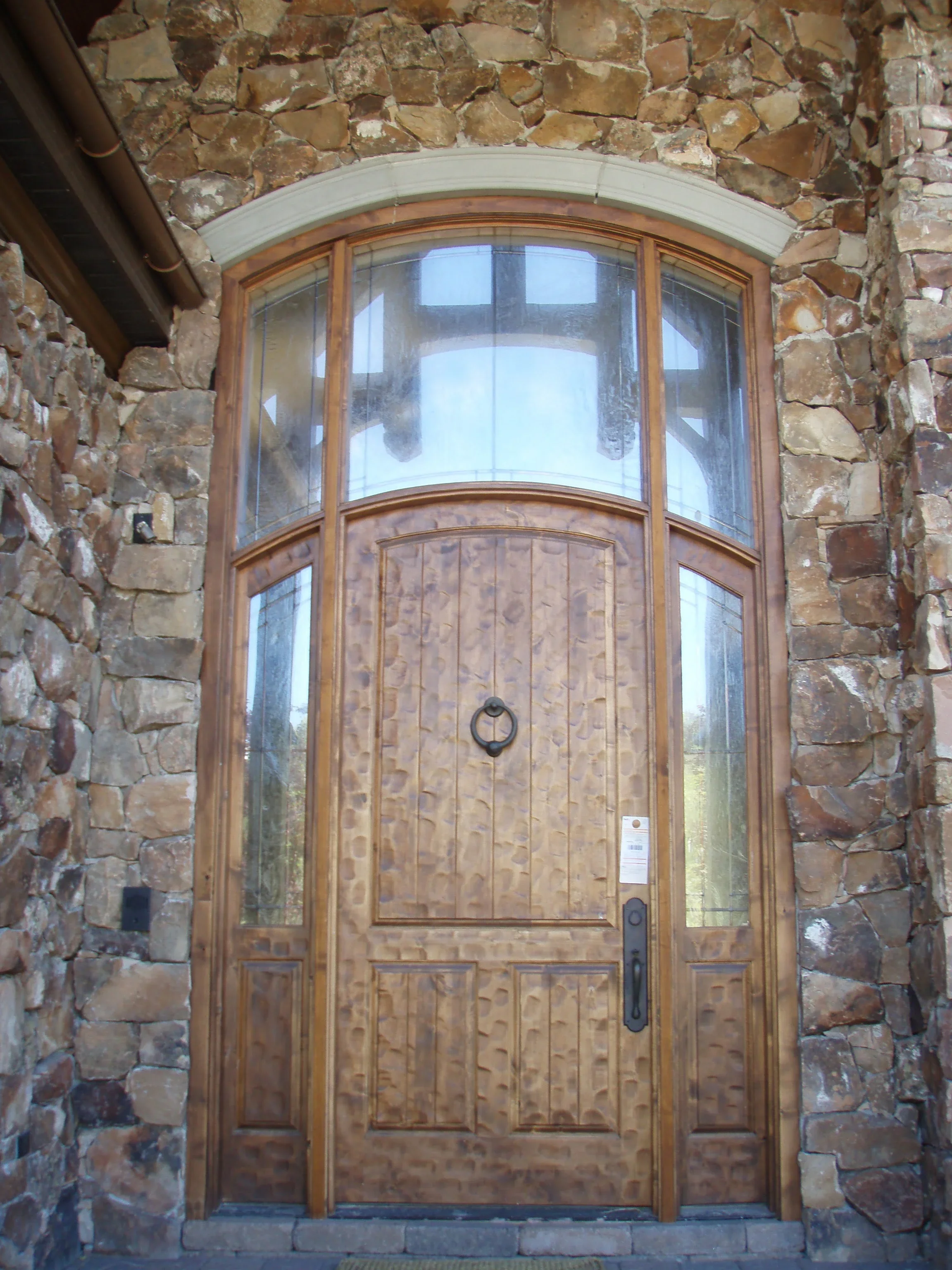 Wooden arched entry door with curved glass sidelights in stone facade